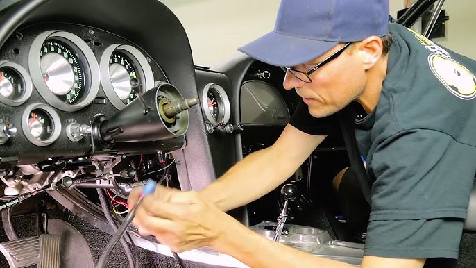 Close-up of a hand on a steering wheel with a car's front suspension and steering rack visible in the background