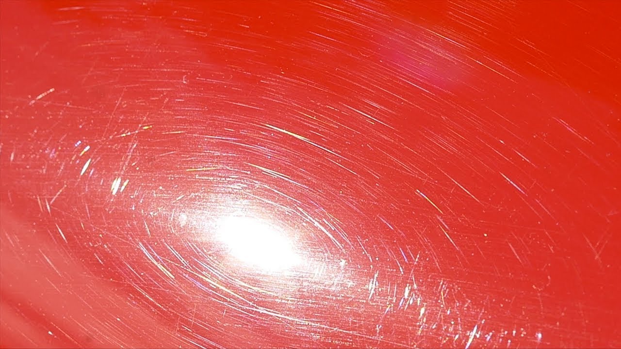 Close-up of a dark car's paint showing fine circular swirl marks reflecting under direct sunlight